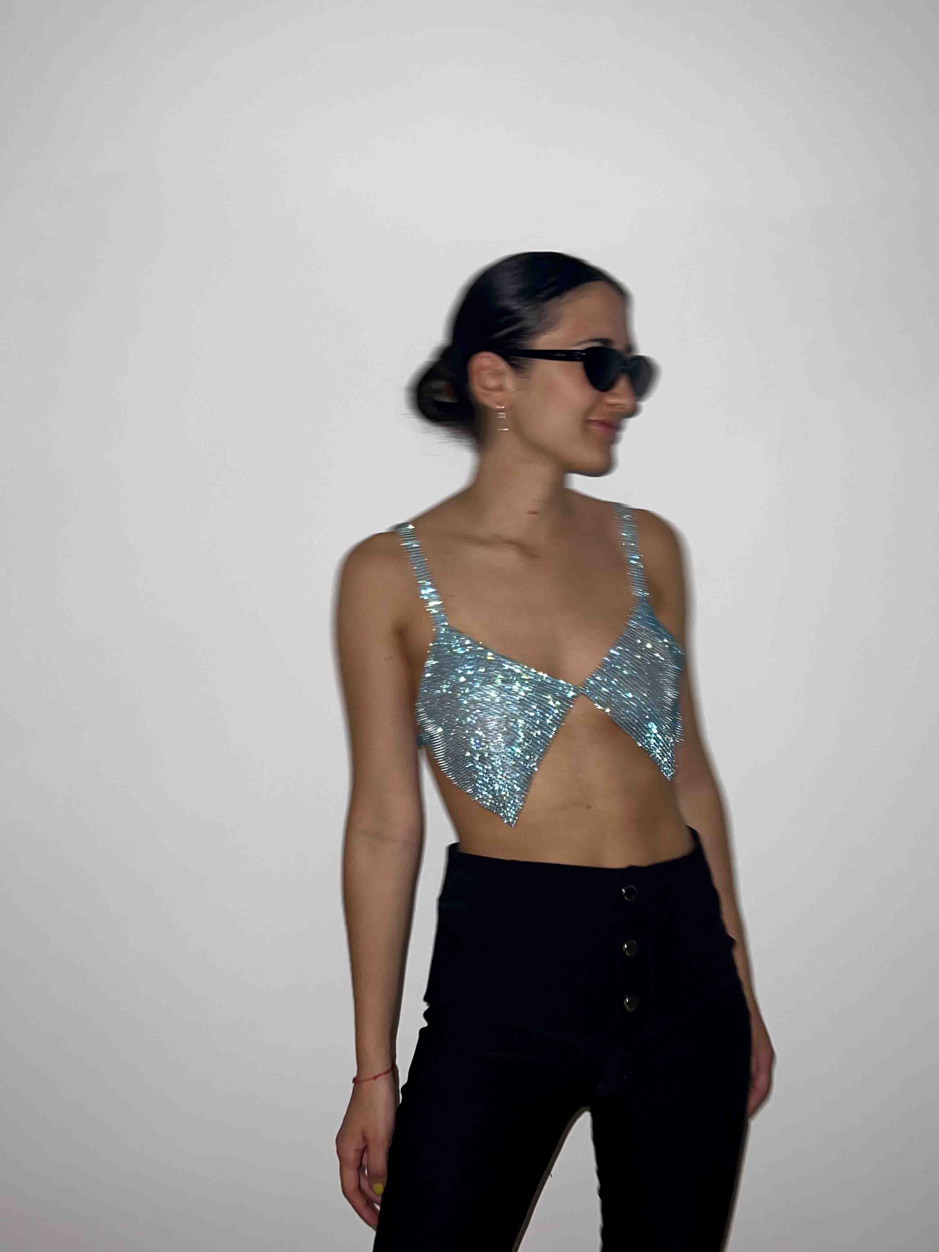 Model wears a chainmail crystal crop top in blue. Embellished bralette top for party clothing and rave festival outfits.