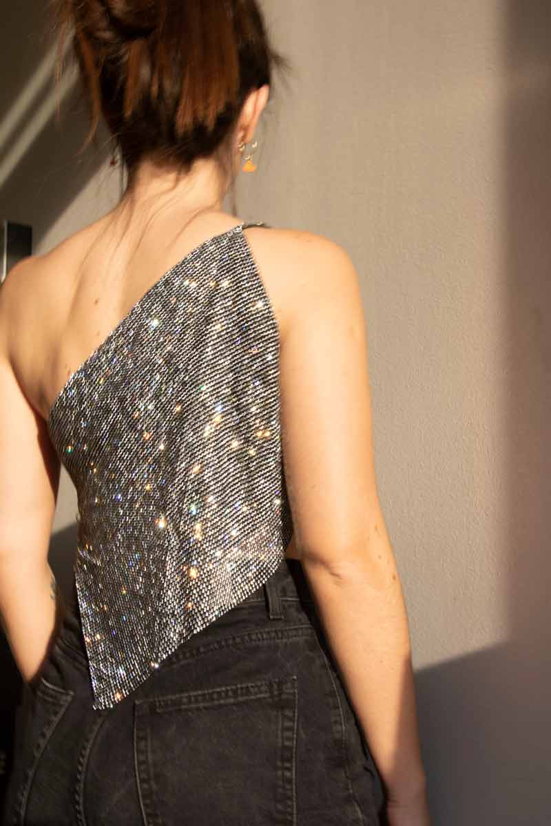 Model wearing a chainmail crystal mesh top in color Black. One shoulder with silver chains on the side. Embellished rhinestone crop top.