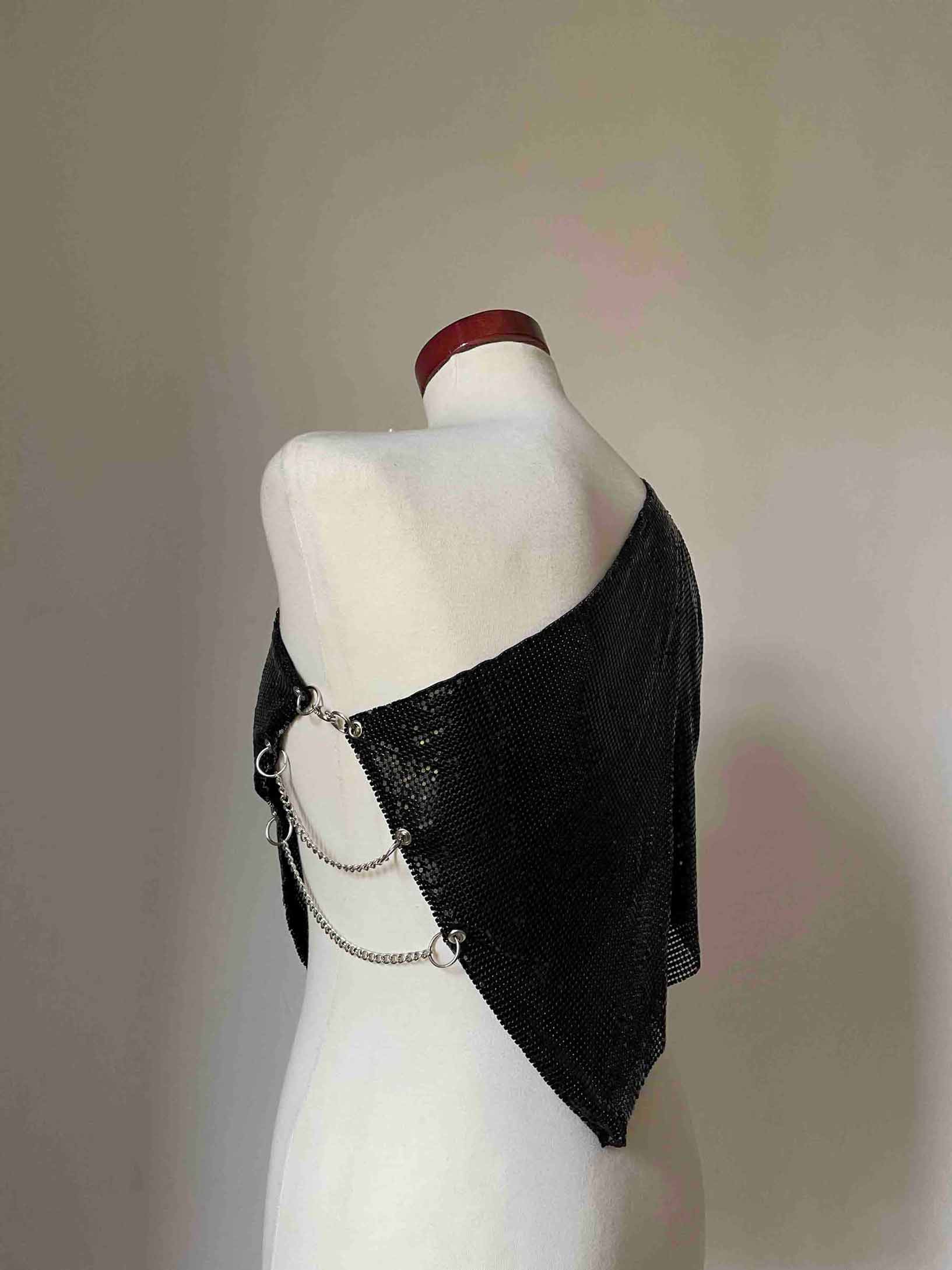 Model wearing a chainmail metal mesh top in color Black. One shoulder with silver chains on the side.